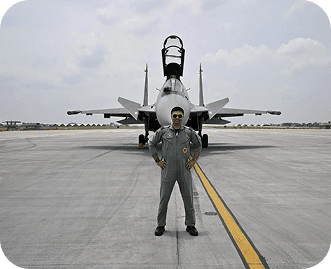 Wg Cdr Pushpendra Dhaka standing on an airstrip in front of a fighter aircraft